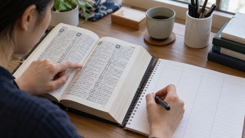 Chinese Last Name Generator: Family Surnames vs Fictional Choices 2 A person reads an open reference book beside a blank notebook